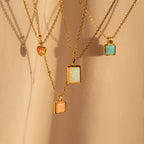 Four gold chain necklaces, including the Pink Opal Pendant Necklace, are displayed on a soft beige fabric background.