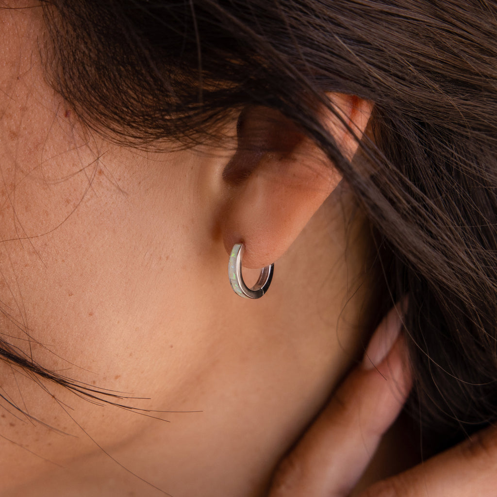 Close-up of a person wearing White Opal Inlay Hoops, small silver earrings partly hidden by dark hair—an elegant option for anyone seeking classic hoops or delicate opal accents.