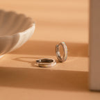 White Opal Inlay Hoops featuring shimmering opal accents rest on a beige surface beside a white ceramic dish—ideal as elegant bridal earrings or for everyday wear.