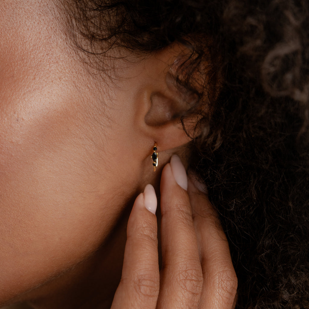 A hand touches the Amaya Black Marquise Threaders—a modern gold earring—worn on an ear with curly hair and natural skin.
