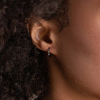 Close-up of a person’s ear wearing Black Sand Opal Huggies—small, silver hoops with embedded opal gemstones, perfect as everyday earrings.