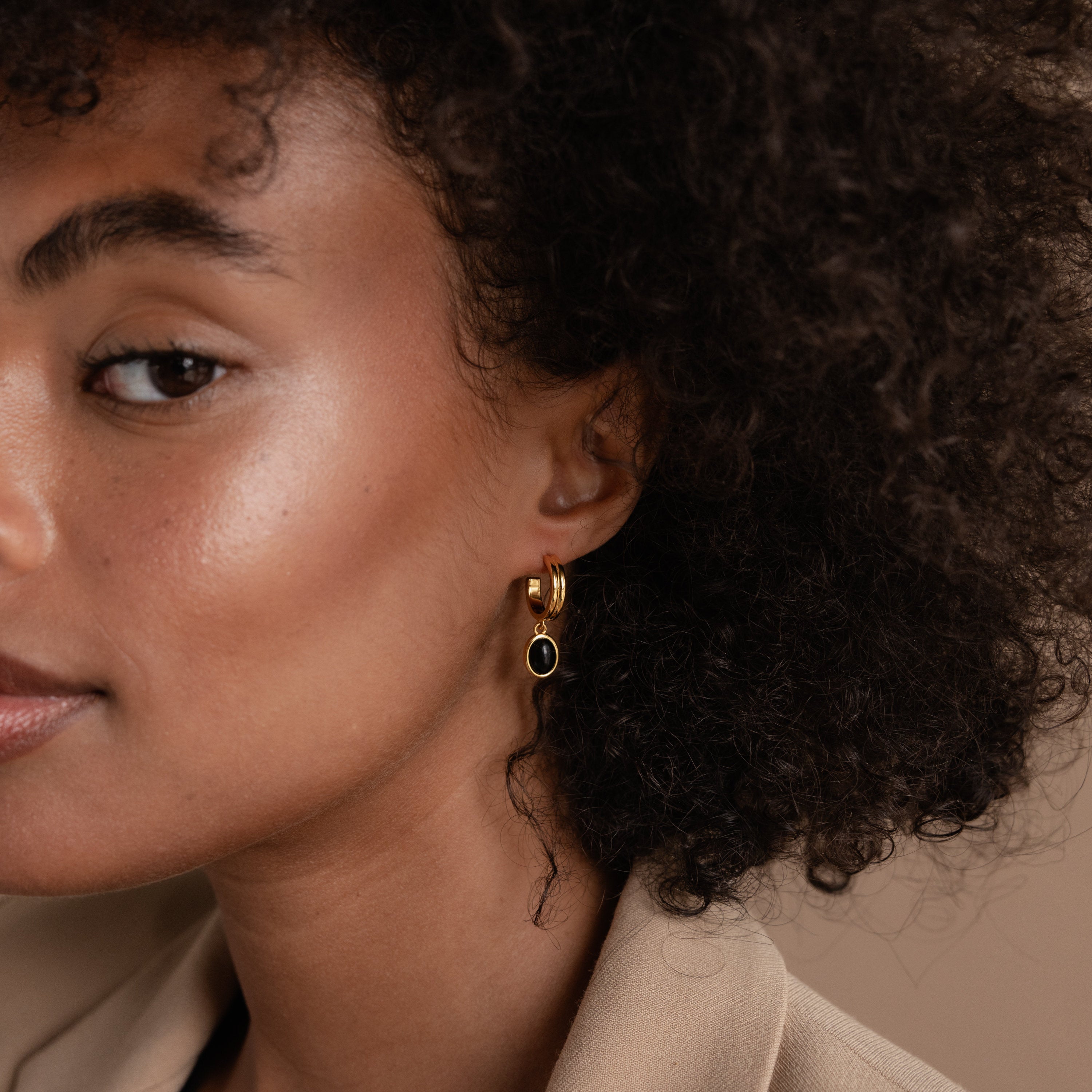 A woman with curly hair wears Black Gemstone Drop Hoops in gold and black, gazing confidently to the side—perfect everyday earrings for making a bold statement.