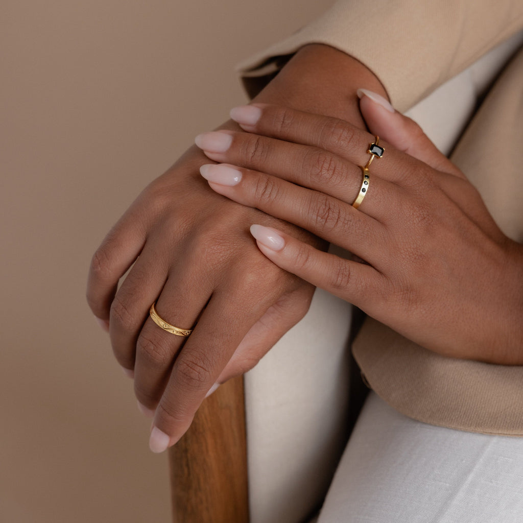 Model showcasing a gold filigree ring on one hand, and an onyx ring paired with a gemstone-accented gold ring on the other, styled against a neutral beige outfit.