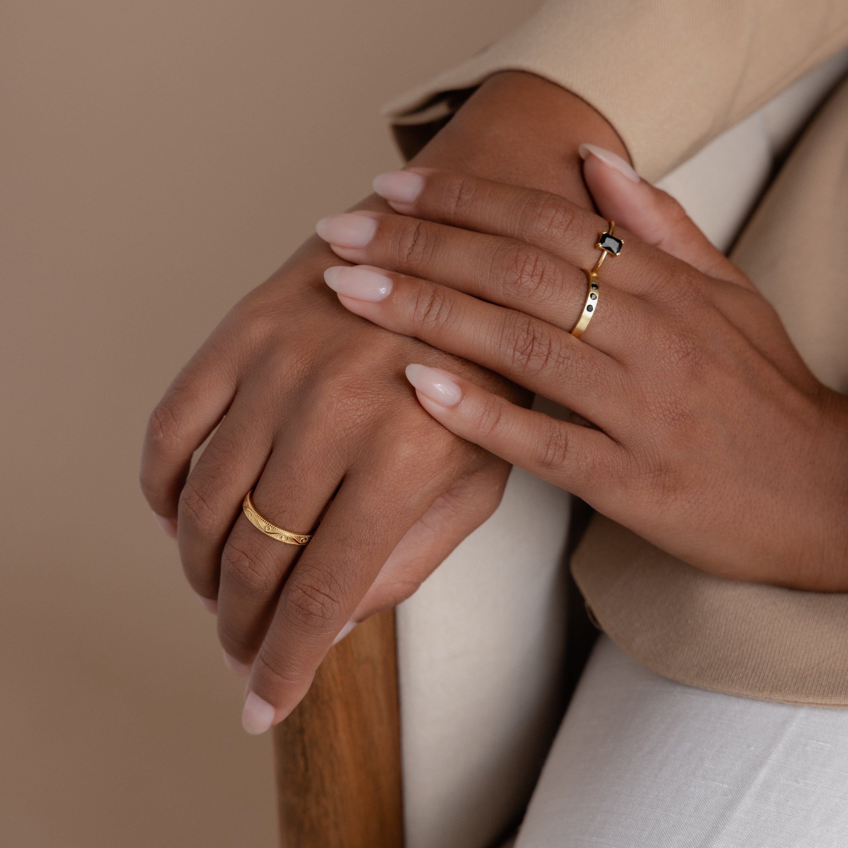 Model showcasing a gold filigree ring on one hand, and an onyx ring paired with a gemstone-accented gold ring on the other, styled against a neutral beige outfit.