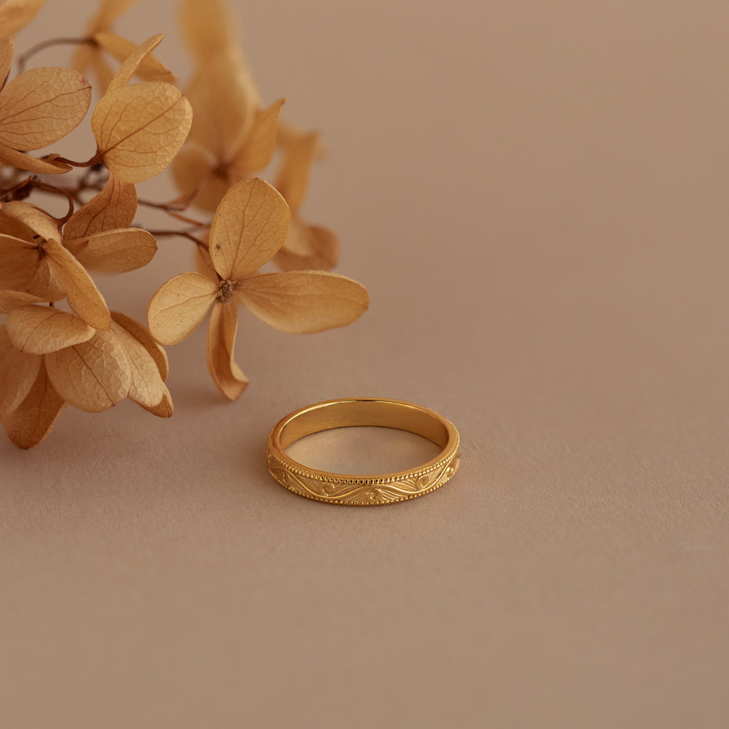 Gold filigree ring placed beside dried blooms, emphasizing the botanical elegance of the engraved band.