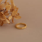 Gold filigree ring placed beside dried blooms, emphasizing the botanical elegance of the engraved band.