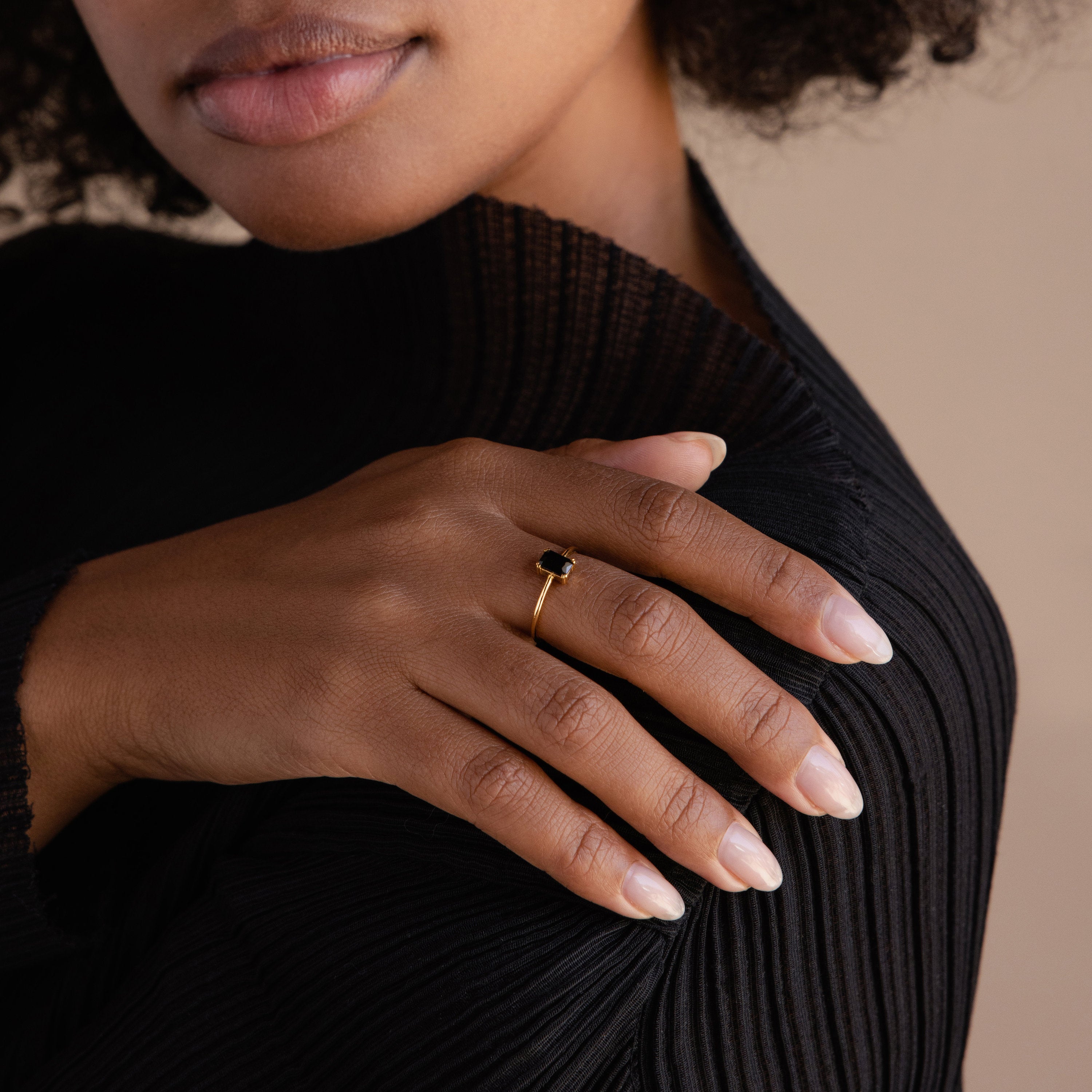 A woman in a black top rests her hand on her shoulder, showcasing the Black Emerald Ring—a vintage-inspired piece featuring a striking black stone.