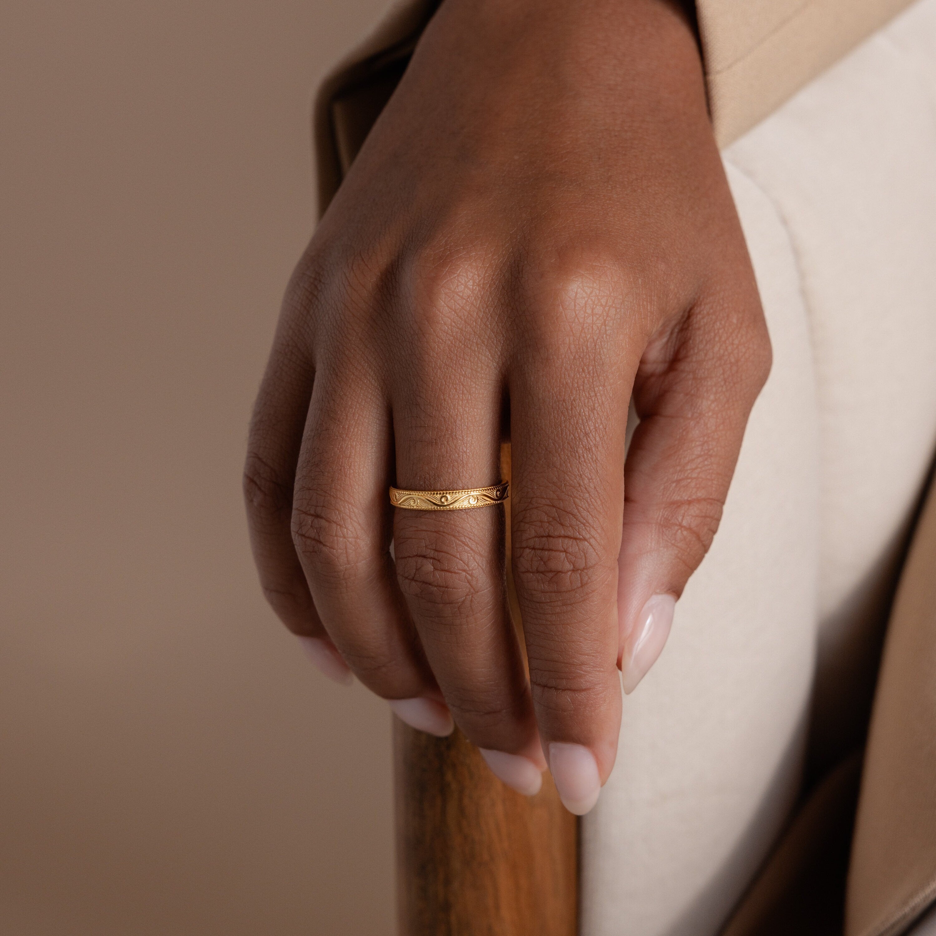 Model’s hand resting on chair arm, wearing a gold filigree ring with vintage swirl.