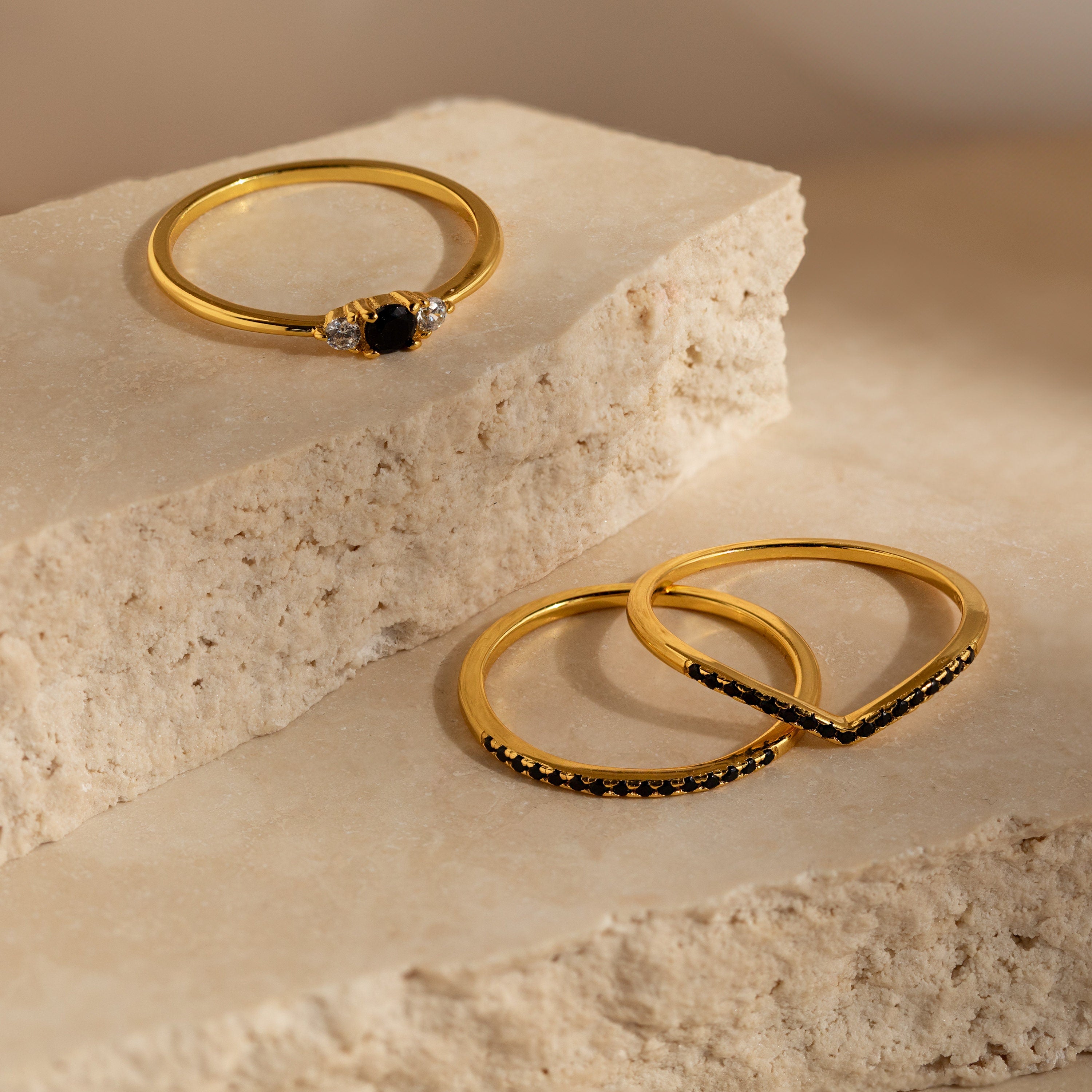 Three Black Curve Ring Sets featuring elegant black stones are displayed on beige stone blocks in soft natural light.