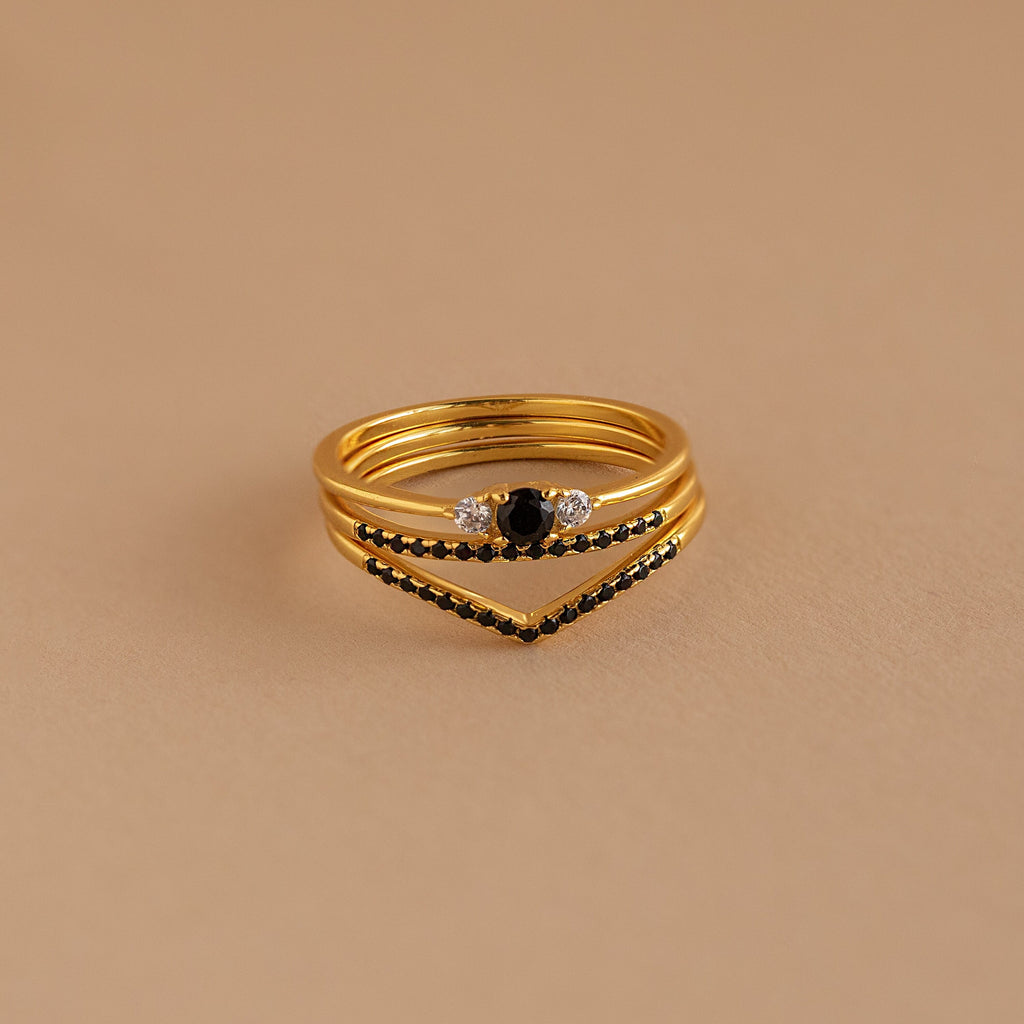 The Black Curve Ring Set showcases black and clear gemstones, including a stylish eternity ring, all stacked elegantly on a neutral beige background.