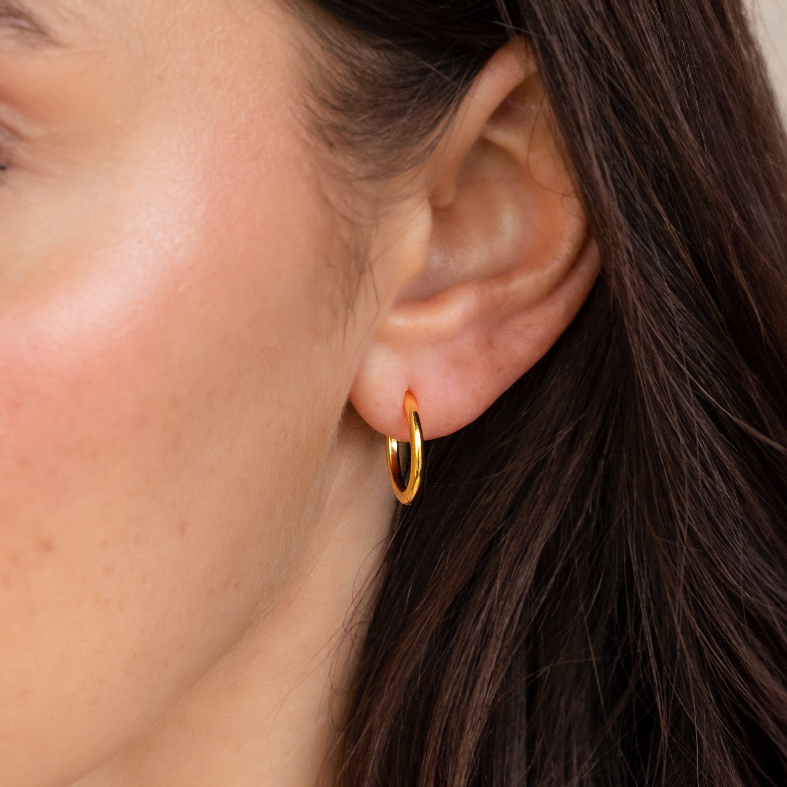Close-up of a person wearing the Mini Bold Hoops Set in their left ear, highlighting the timeless charm of these classic gold earrings.