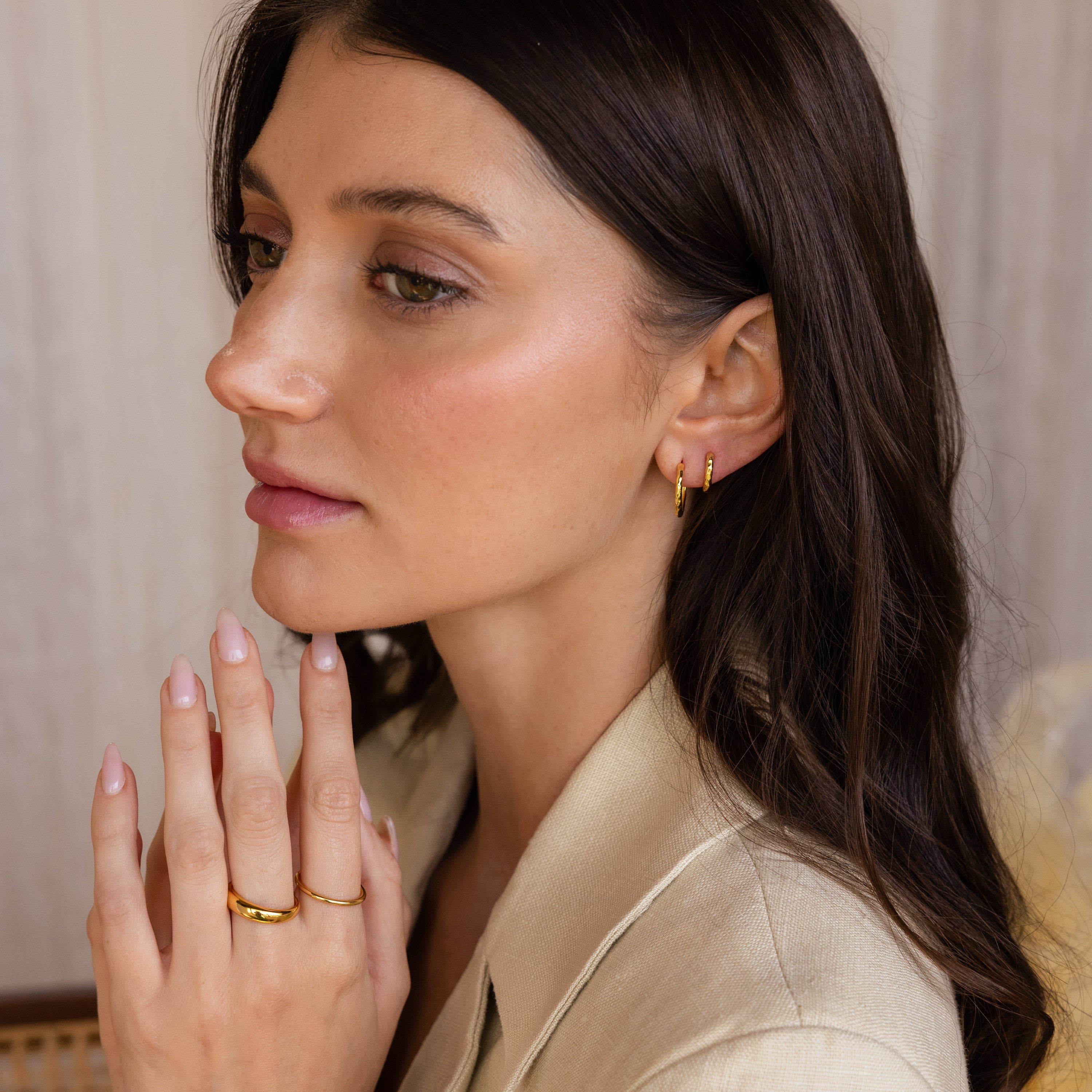 A woman with long brown hair gazes thoughtfully to the side, accessorized with the Mini Hammered Hoops Set.