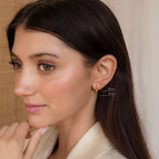 A woman with long brown hair wears two small gold hoop earrings from our Mini Bold Hoops Set, labeled 10mm and 12mm, on her left ear.