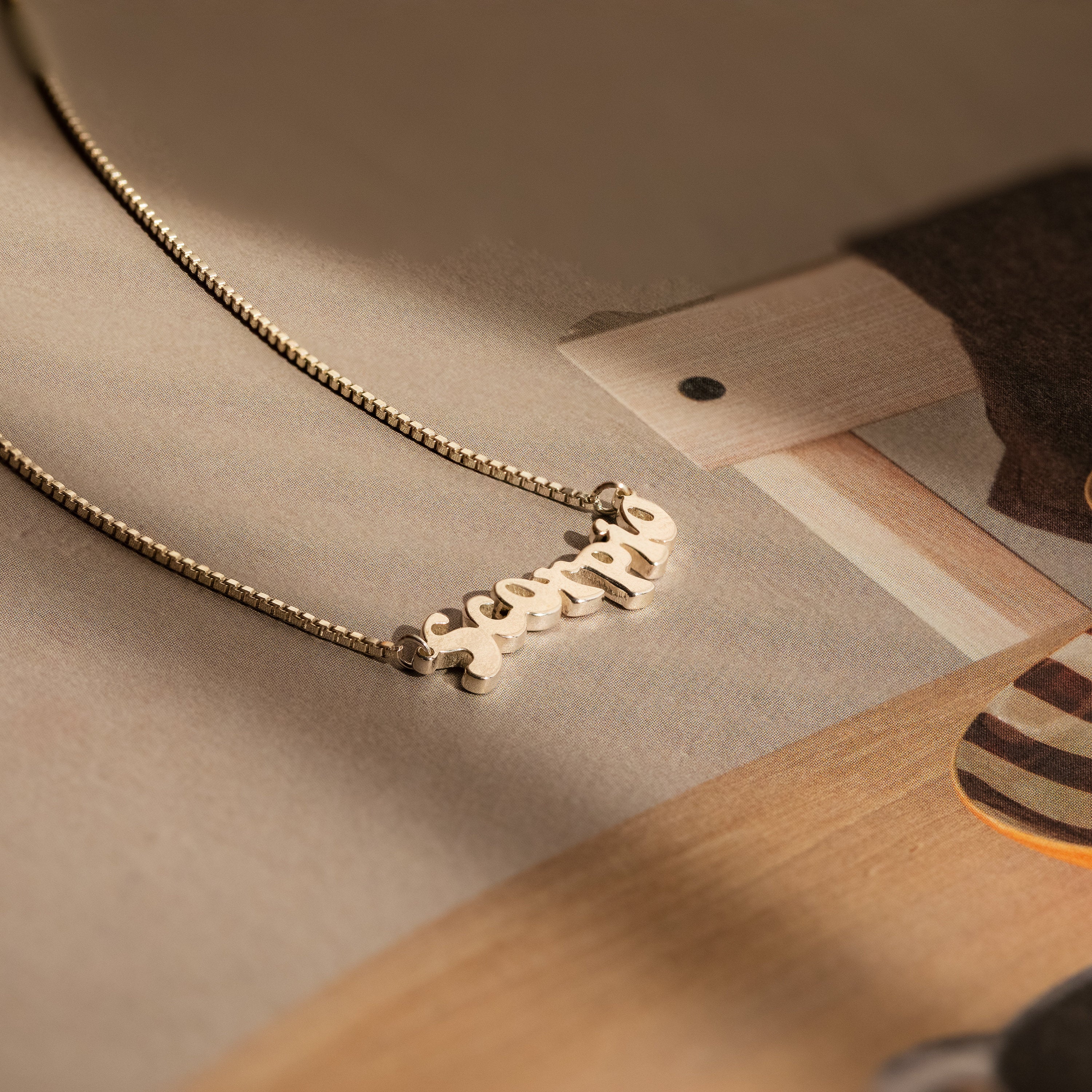 Retro Name Necklace in Box Chain showcased on a gently lit beige surface—an elegant, personalized jewelry piece ideal for expressing your distinct style.