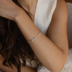 A woman rests her arm on a soft, textured surface while wearing a delicate Mini Name Birthstone Bracelet.