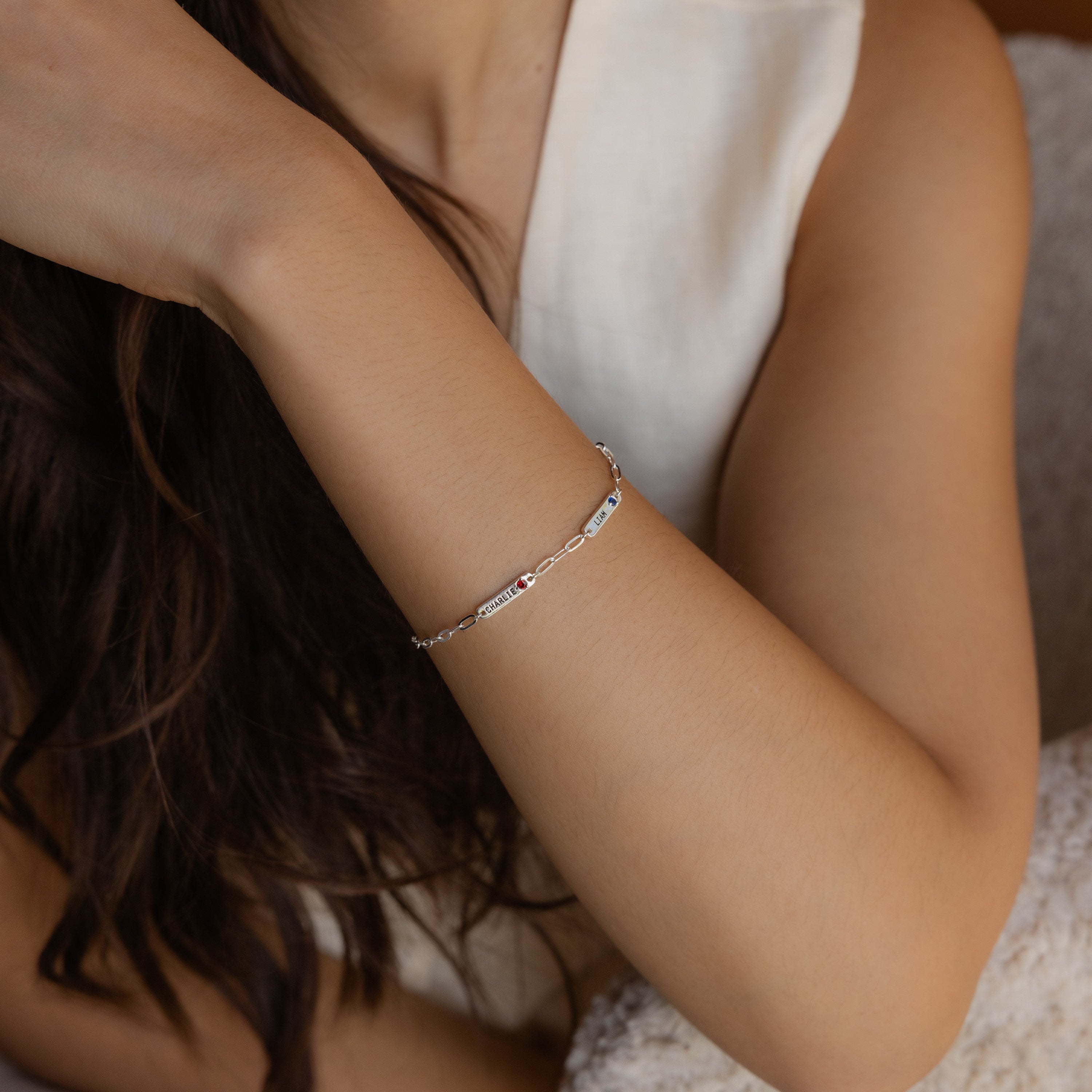 A woman rests her arm on a soft, textured surface while wearing a delicate Mini Name Birthstone Bracelet.