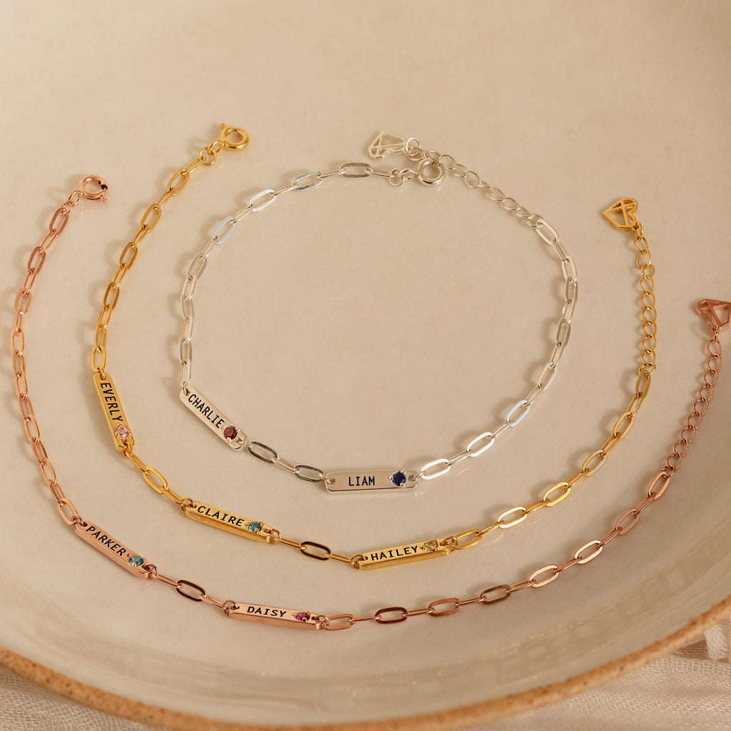 Five Mini Name Birthstone Bracelets, including paperclip styles, elegantly displayed on a beige ceramic plate—perfect as a customized gift.
