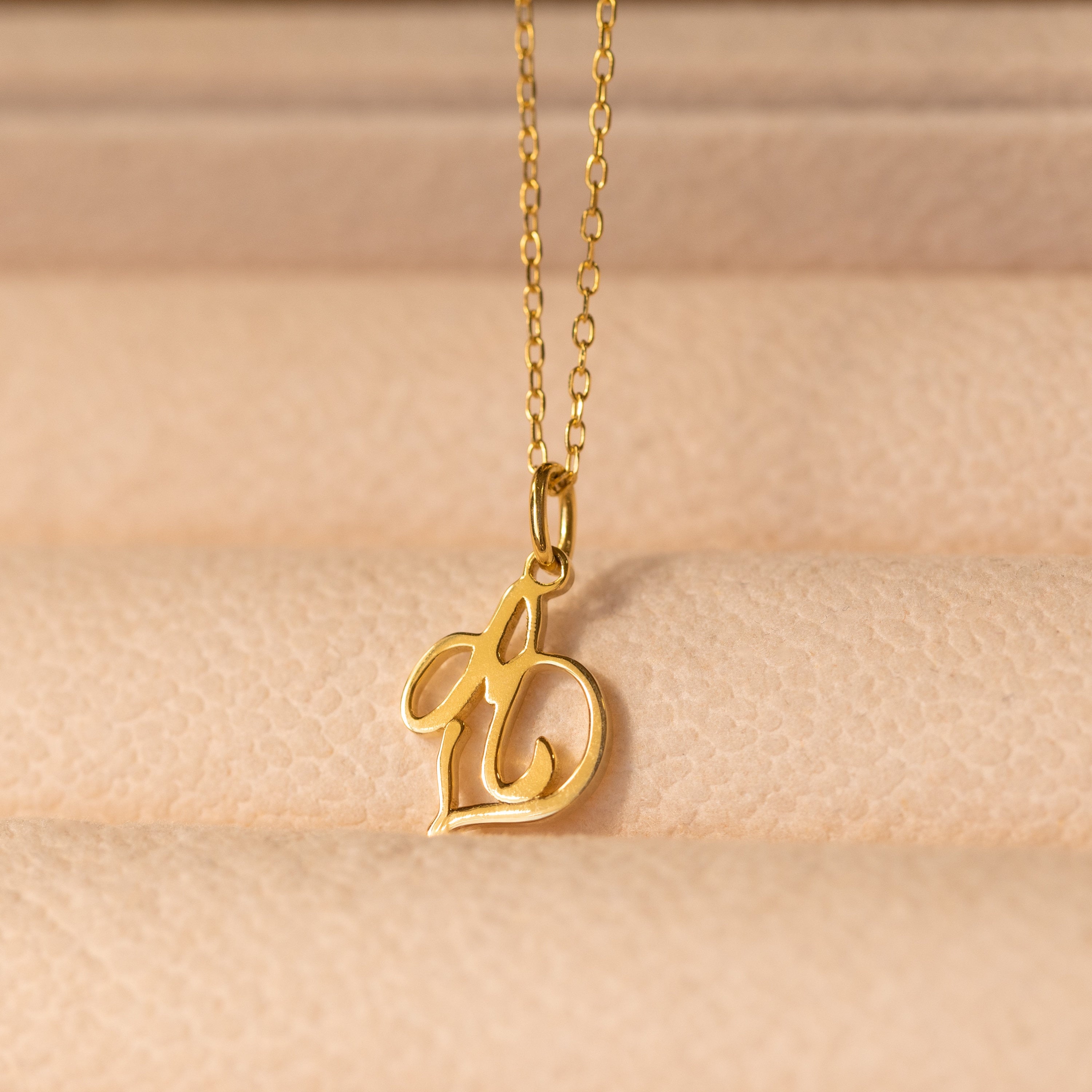 Initial Heart Necklace featuring a cursive letter b pendant on a soft beige textured surface—a beautiful custom piece and the perfect gift for someone you love.