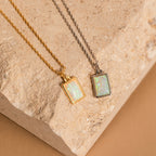 Two White Opal Rectangle Necklaces, ideal for a charm necklace or bridal jewelry, are displayed on gold and silver chains over a textured beige stone surface.