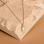 The White Opal Rectangle Necklace showcases a silver chain with a rectangular opal pendant, elegantly displayed on textured beige stone—ideal as bridal jewelry or to add everyday sophistication to your look.