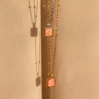 Two minimalist Pink Opal Pendant Necklaces, one in silver and one in gold, hang on satin satellite chains against a soft beige fabric background.