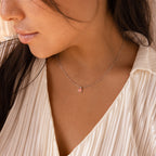 A woman in a pleated cream blouse wears the Pink Opal Pendant Necklace—a delicate satellite chain with a pink rectangular pendant.