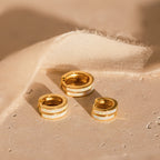 Three White Opal Inlay Huggies are displayed on a light textured surface next to beige fabric.