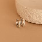 White Opal Inlay Huggies are displayed on a tan surface next to a textured beige stone.