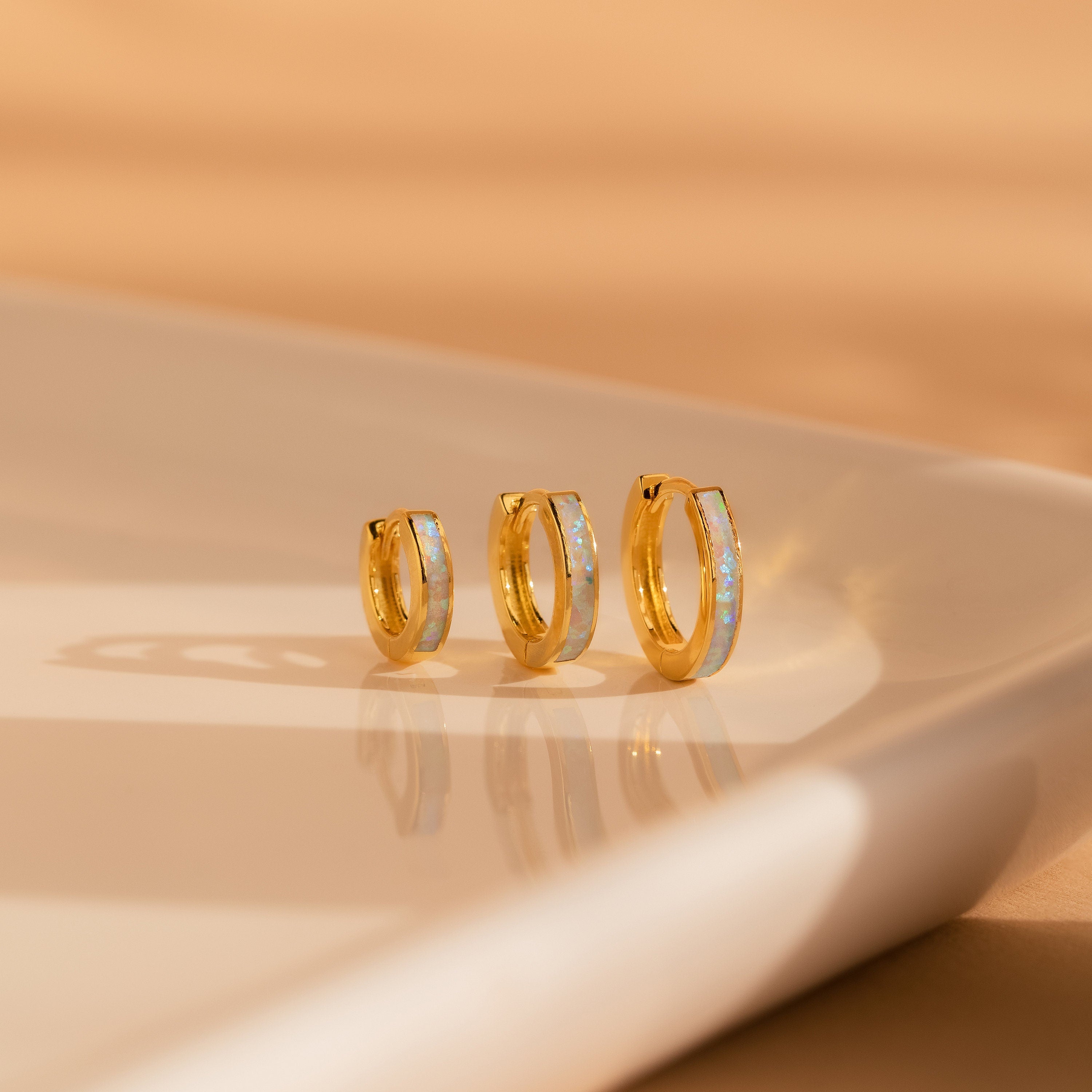 The White Opal Inlay Hoops, shown in three sizes on a white ceramic surface with a beige background, add a classic touch to any look and are also an elegant choice for bridal earrings.