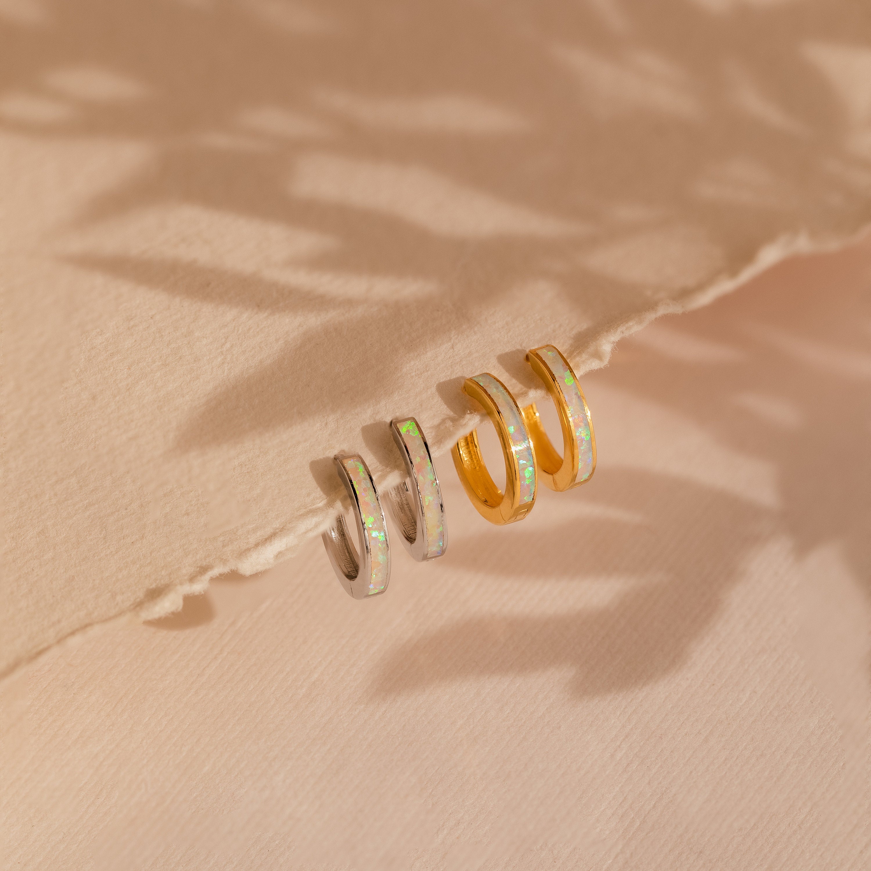 Two pairs of White Opal Inlay Hoops—one silver, one gold—are displayed on a textured beige surface. Ideal as bridal earring accents or chic hoops for any occasion.