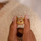 A hand displays the Tiny Cluster Birthstone Ring, a stackable set with red and white gemstones and a customizable birthstone, against a neutral background.