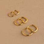 The Mini Bold Hoops Set—three pairs of classic hoops in small, medium, and large—are arranged on a beige surface.
