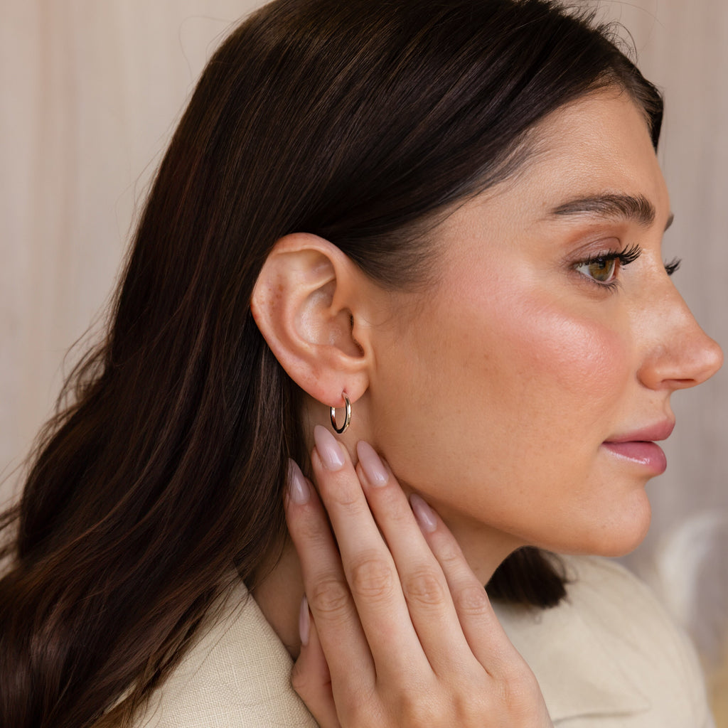 A woman with manicured nails touches her neck, shown in profile view while wearing the Mini Bold Hoops Set.