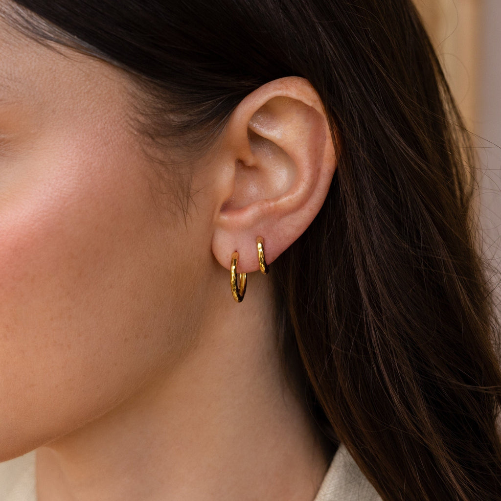 Close-up of a woman's ear with two Mini Hammered Hoops and long brown hair, highlighting the elegance of these gold or silver hoop earrings.