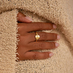 A hand with manicured nails wears the Initial Birthstone Signet Ring, resting on a textured beige sweater.