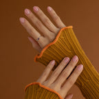 Hands with light pink nails wear the Irregular Baguette Birthstone Ring, paired with mustard ribbed sleeves, set against a brown background.