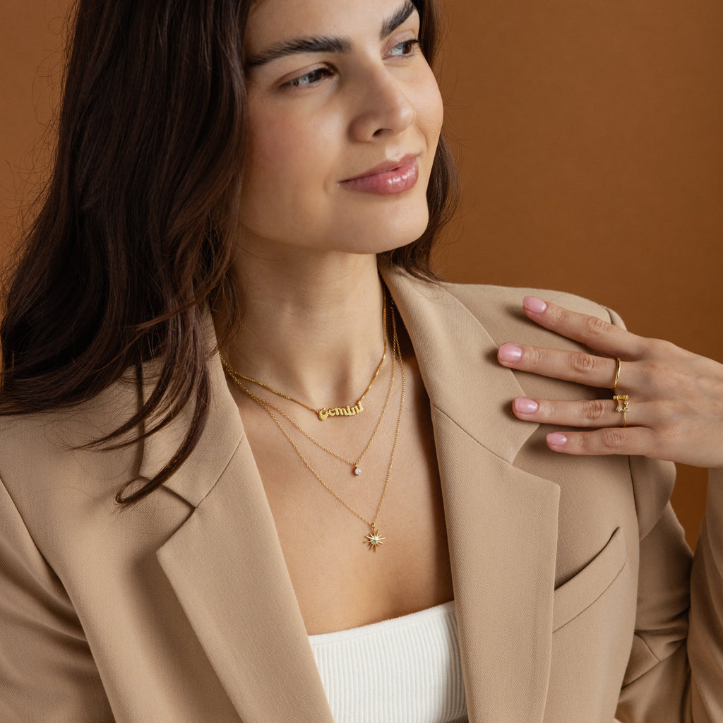 A woman wears a tan jacket paired with the Retro Name Necklace in Box Chain, adding a personalized touch to her look.