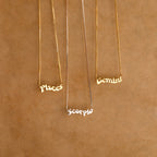 Three Retro Name Necklaces in Box Chain with Pisces, Scorpio, and Gemini pendants rest on a brown textured background—ideal custom charm jewelry for anyone who loves personalized pieces.