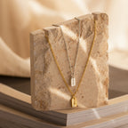 The Tiny Initial Tag Necklace, shown in both silver and gold on a textured stone slab with a neutral backdrop, is ideal for those who appreciate elegant, personalized jewelry.
