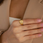 A hand with pink nails wears the Lucky Number Signet Ring, engraved with 96, touching a beige blazer—ideal statement jewelry for fans of personalized engraving.