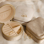 The Mystery Jewelry Box in beige and cream velvet, with one open to reveal rings, is displayed elegantly on a marble surface.