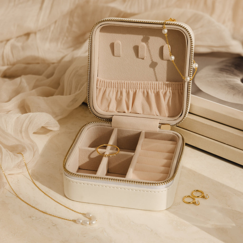 The Mystery Jewelry Box displays handpicked rings, a pearl necklace, and gold earrings on a beige fabric background.