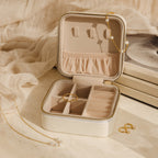 The Mystery Jewelry Box displays handpicked rings, a pearl necklace, and gold earrings on a beige fabric background.