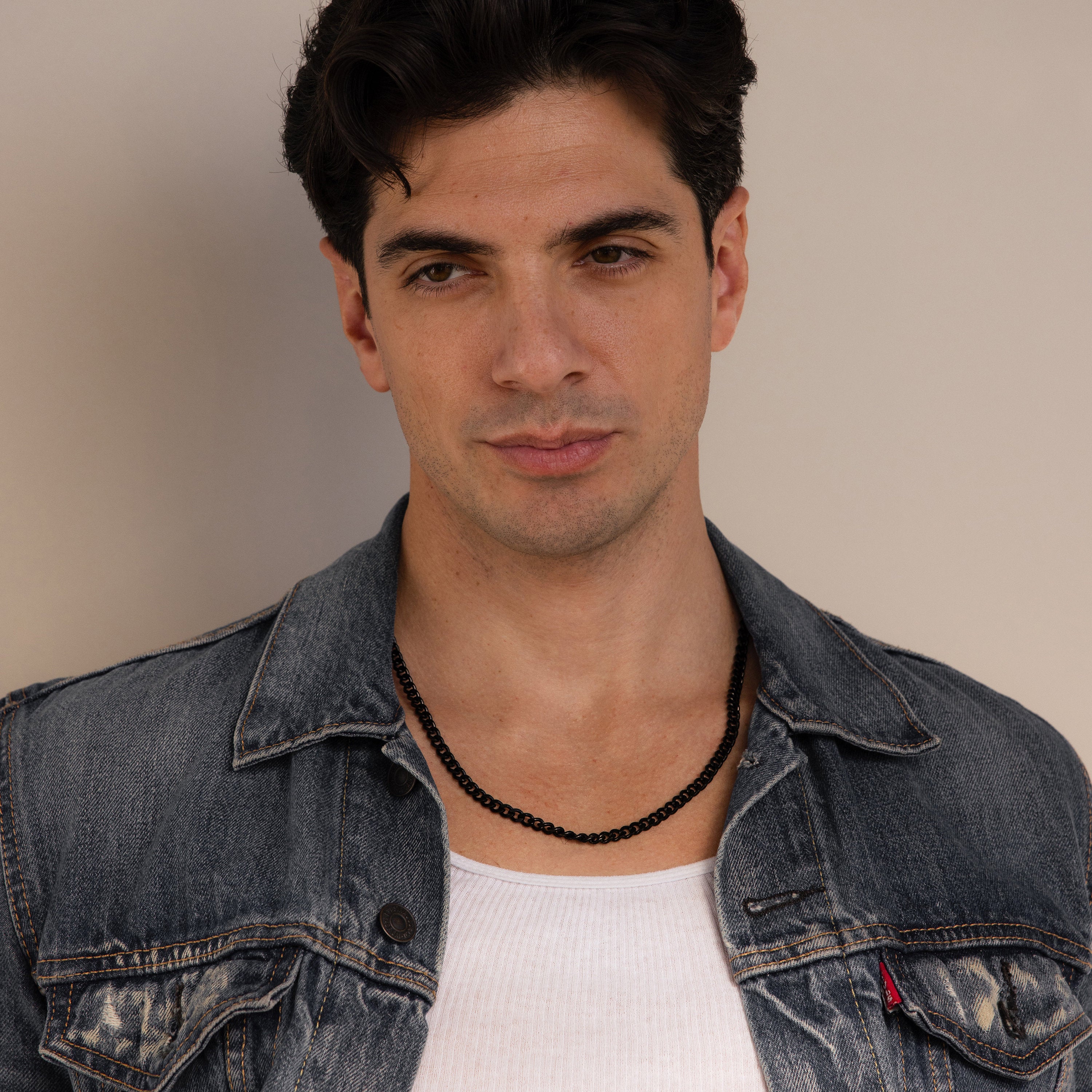 Man with dark hair in a denim jacket and white shirt wears the Men's Black Curb Chain, looking at the camera. A bold statement necklace—an ideal stylish gift for men who love standout accessories.