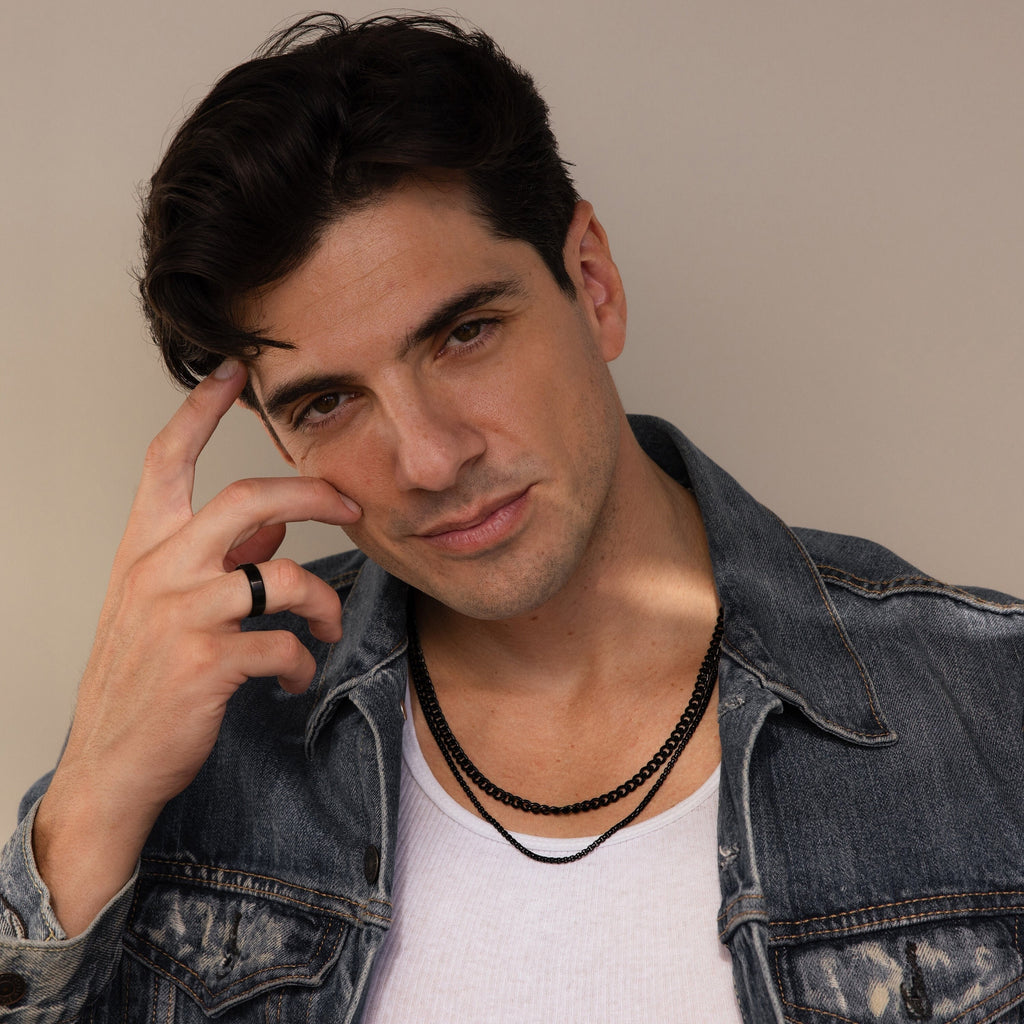 A man in a denim jacket and white shirt poses confidently with his hand near his face, wearing the Men's Black Curb Chain—a standout accessory and an ideal gift for men who appreciate bold style.