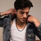 A man in a denim jacket and white tank top adjusts his jacket while looking down, highlighting the Men's Black Curb Chain—a bold statement necklace and ideal gift for men.