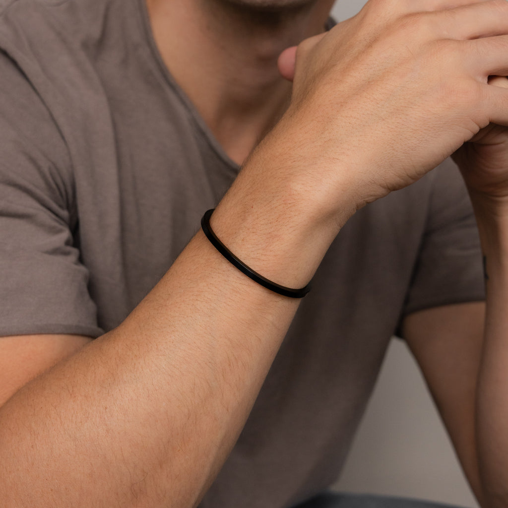 A man wearing the Men's Black Cuff Bracelet and a brown T-shirt, hands near his face—an ideal gift for him.