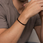 A man wearing the Men's Black Cuff Bracelet and a brown T-shirt, hands near his face—an ideal gift for him.
