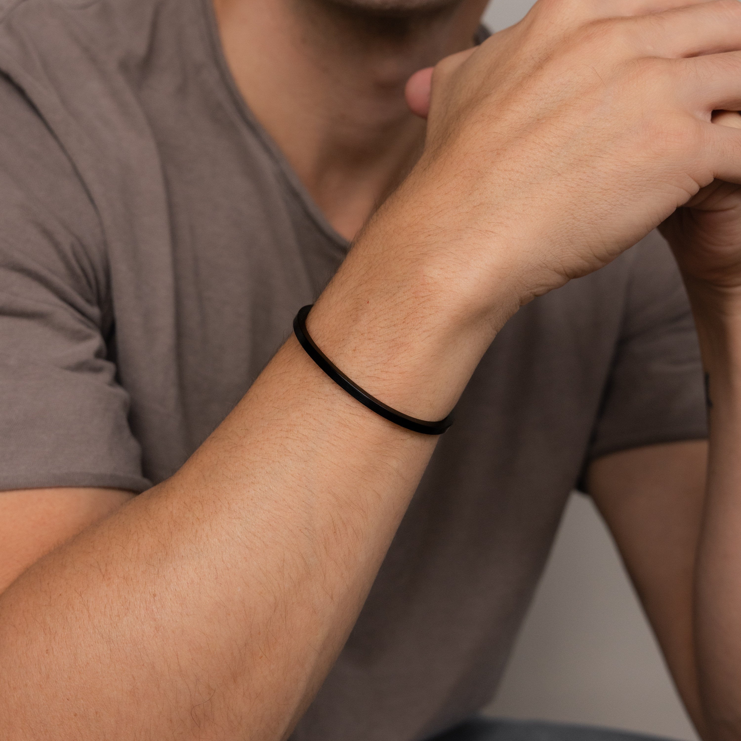 A man wearing the Men's Black Cuff Bracelet and a brown T-shirt, hands near his face—an ideal gift for him.