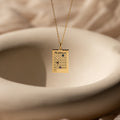 The Calendar Birthstone Necklace features a rectangular calendar-shaped pendant, elegantly displayed above a white ceramic bowl.